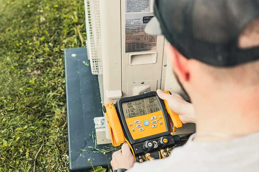 HVAC technician handling ductless mini split repair while measuring system performance at the outdoor unit